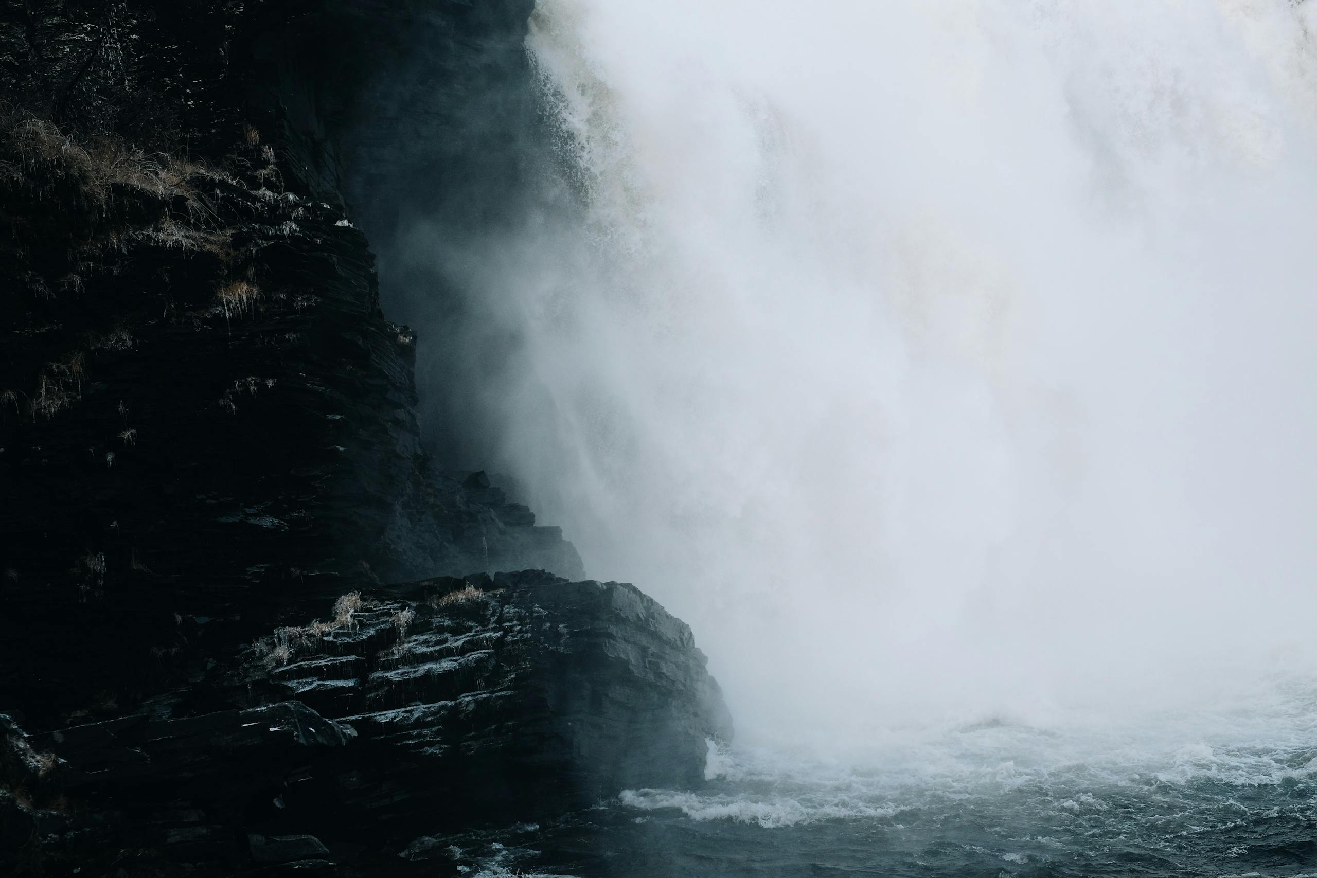 Moody waterfall with dramatic mist cascading over dark rocky cliffside.