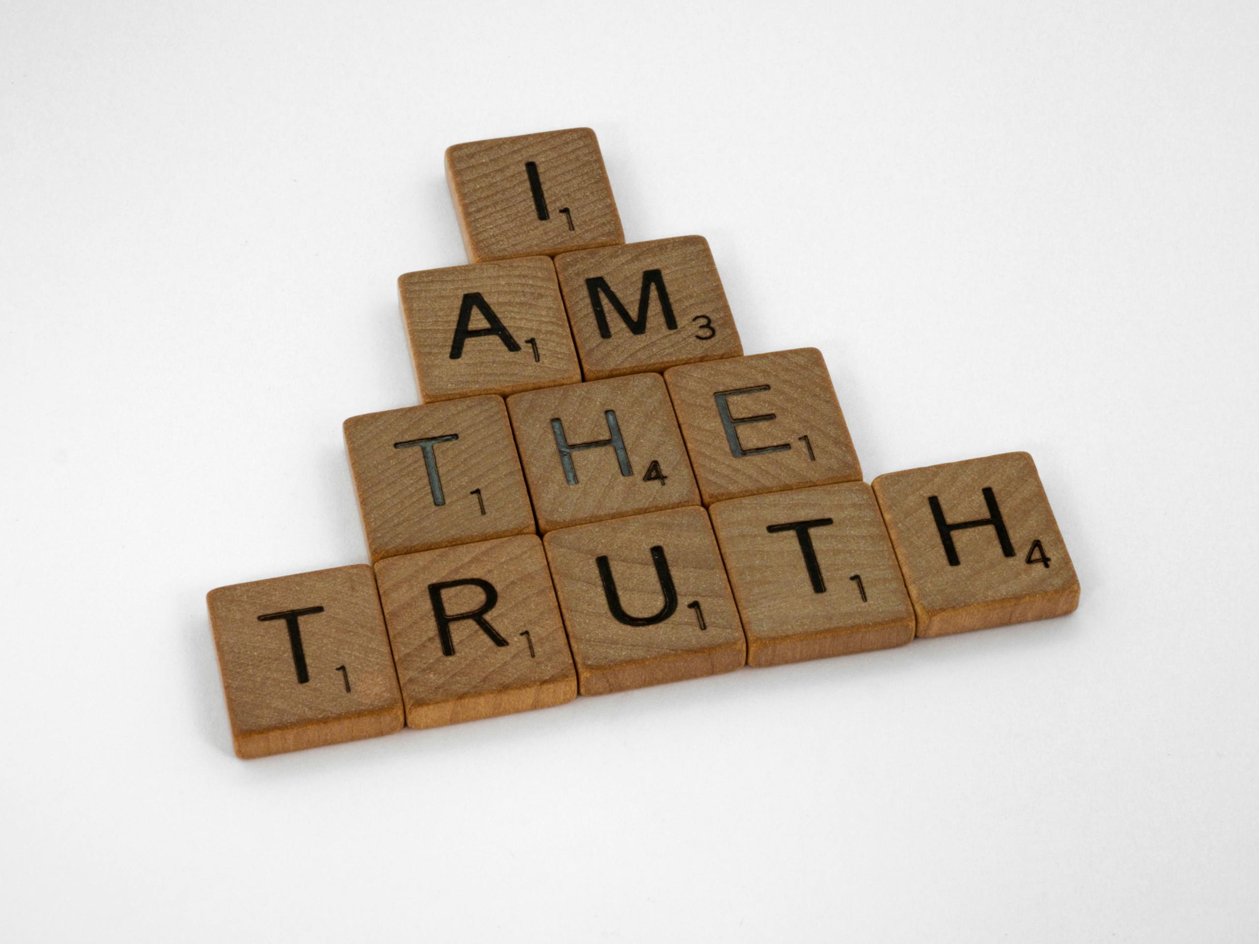 Scrabble tiles arranged on a white surface to spell 'I Am The Truth' in a pyramid shape.